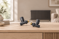Pair of anthracite straight manual radiator valves with brass connectors on a pale oak surface